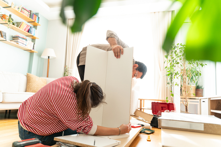 Young couple just married assembling a piece of furniture in their home. With screwdriver and tools in hand to follow the instruction book. Handyman couple. They are the owner.New house, new furniture