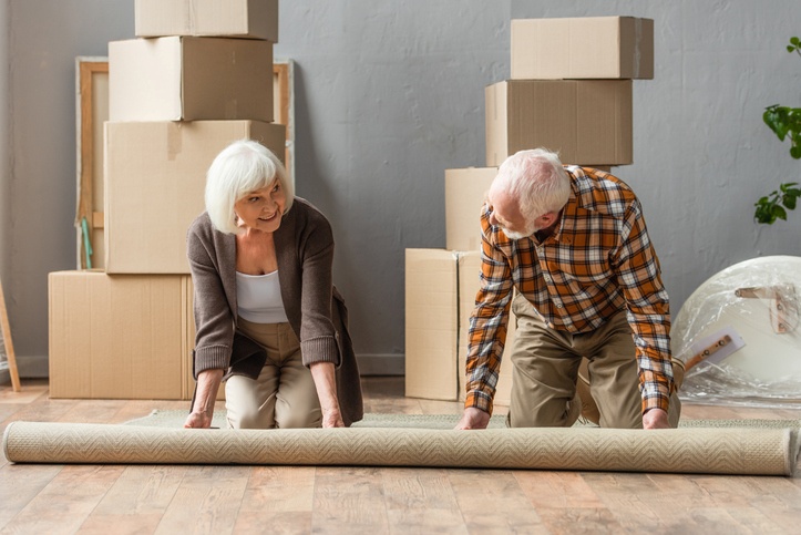 A couple rolling up their rug on the floor.