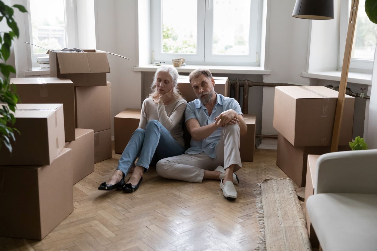 A couple sitting on the floor around all of their cluttered boxes.
