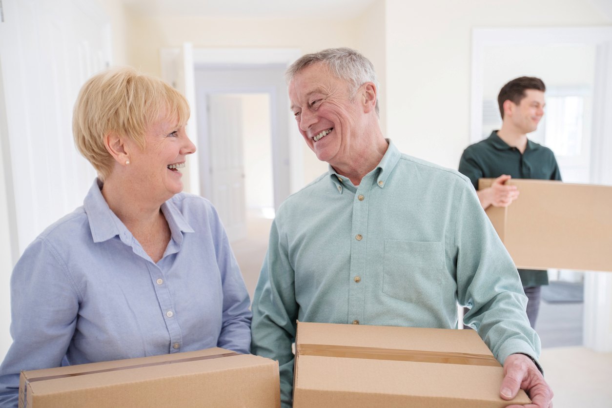 A couple holding moving boxes with a mover working behind them.