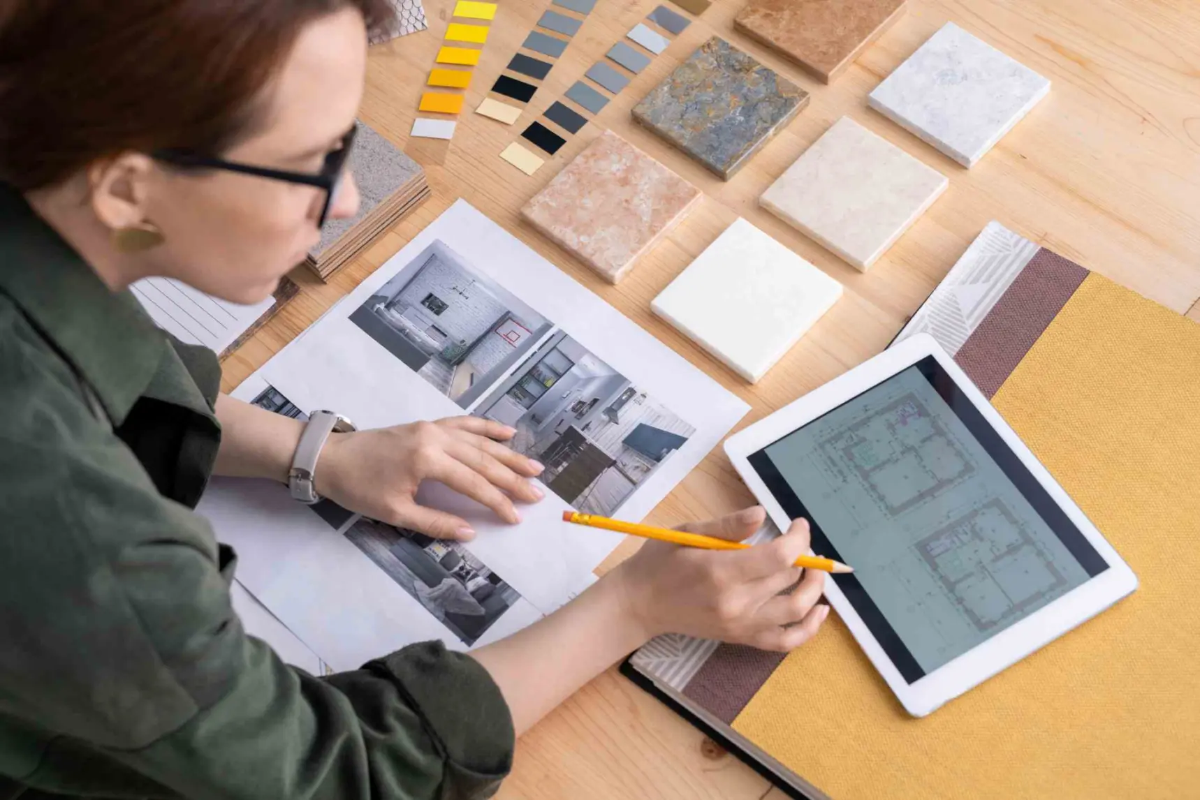Contemporary young female designer of interior bending over desk while looking through electronic sketches of flat in touchpad