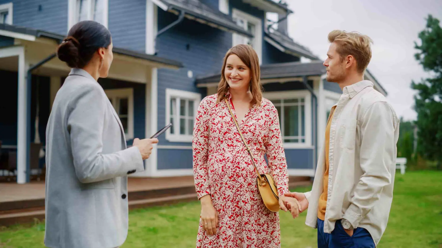 Professional real estate agent Showing a Hot Property Location to a Young Successful Couple. Female Real Estate Agent with Tablet Walking with Family to the House. New Homeowners. Slow Motion