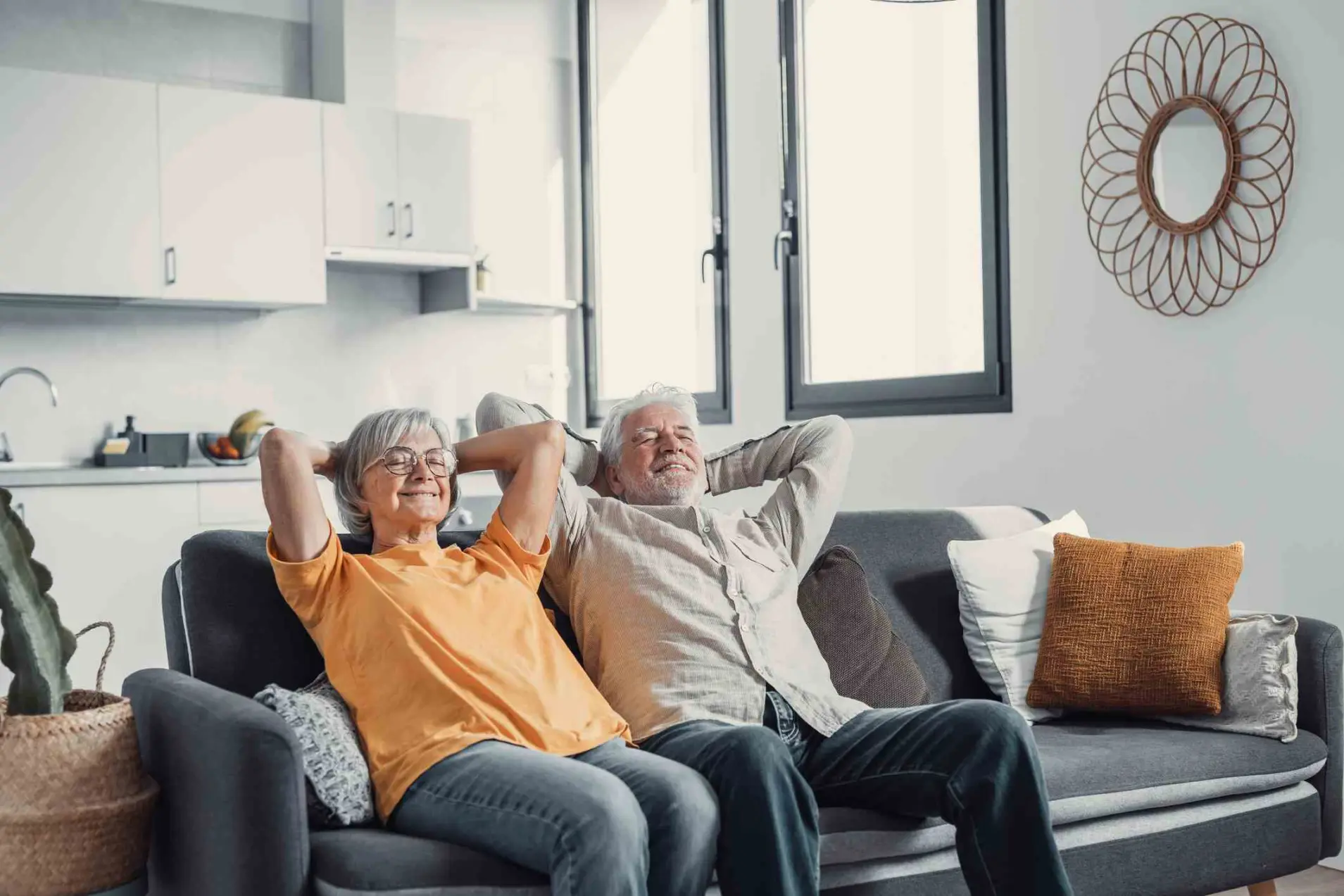 Peaceful middle aged man and woman with closed eyes relaxing on comfortable couch at home, mature family daydreaming together, grey haired wife and husband resting with hands behind head, breathing