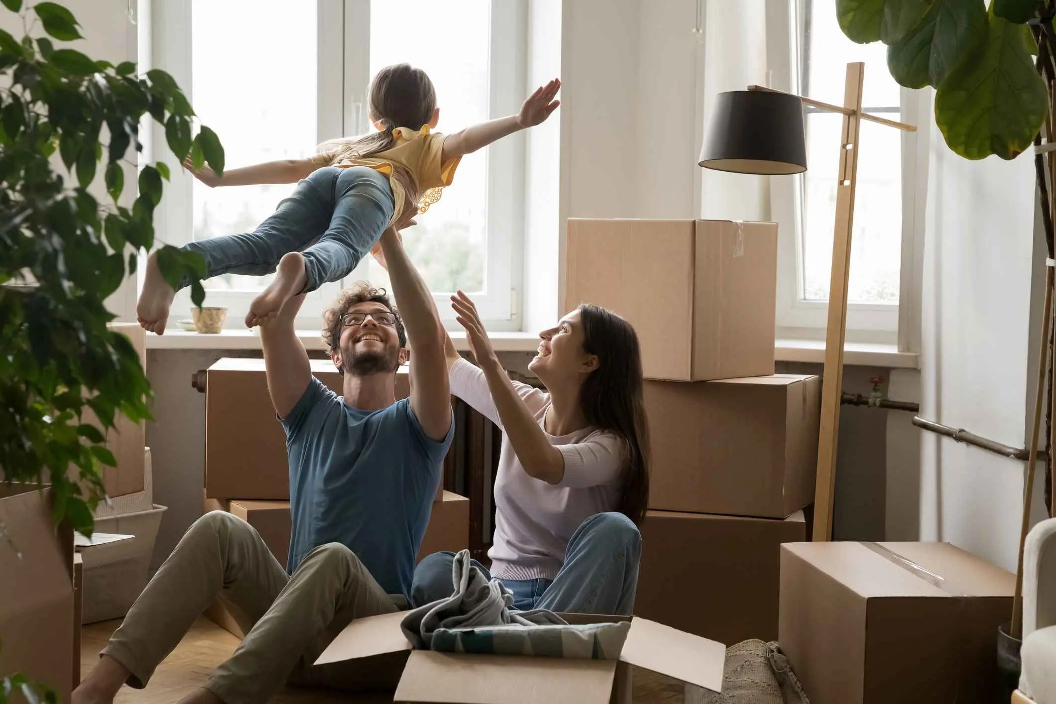Cheerful young loving family with cute little daughter celebrate moving day, having fun, playing with cute little kid, feel happy at new house, sit on floor near heap of boxes. Bank loan, relocation