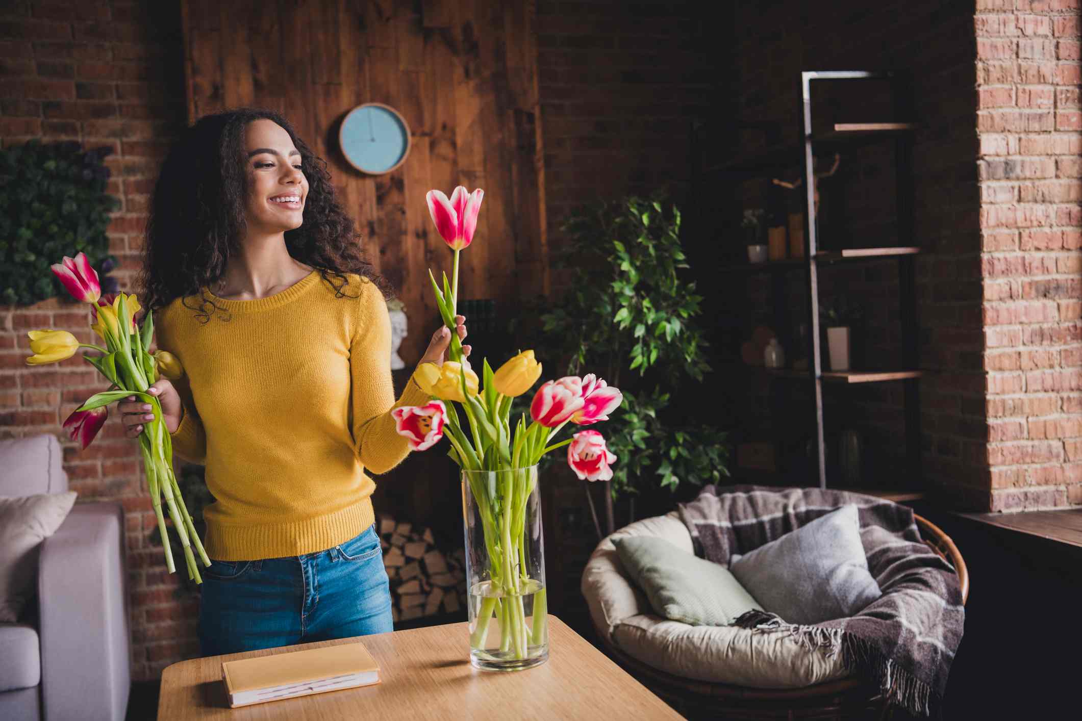 Young afro-american woman arranging tulips in a vase at home, enjoying natural light in a relaxed, modern setting.