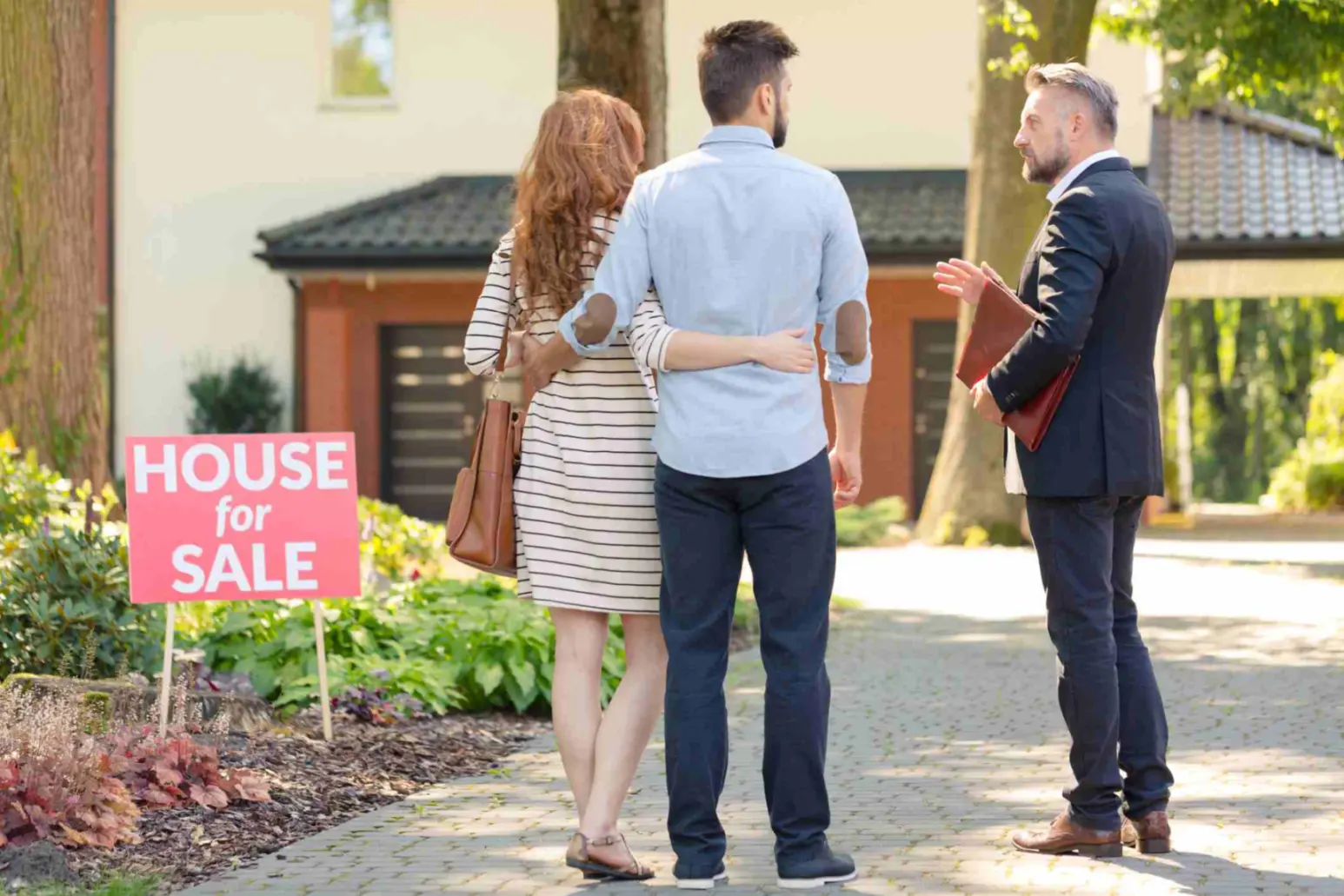 Real estate broker and clients standing next to plate with inscription "house for sale"