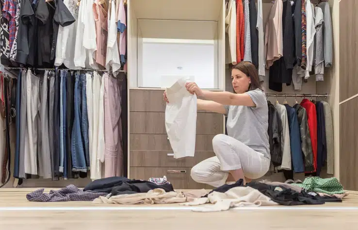 Young woman throwing clothes in walk in closet. Mess in wardrobe and dressing room concept