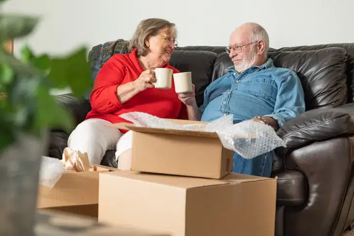 Tired Senior Adult Couple Resting on Couch with Cups of Coffee Surrounded with Moving Boxes.