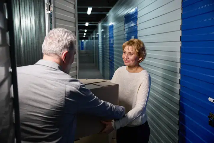 Male holding cartoon box, in storage service, giving cargo to woman in storage room