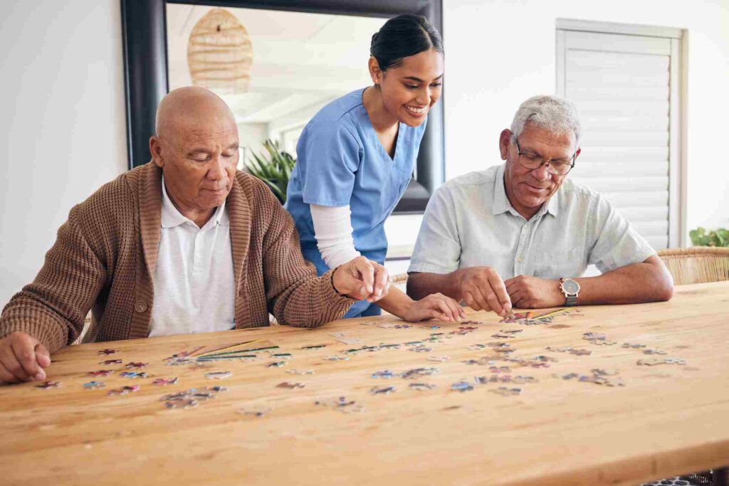 Two senior gentlemen do a puzzle together in senior living with a nurse between them.