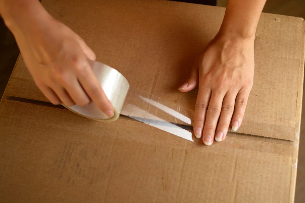 A professional packer places a strip of tape on a cardboard box during the moving process.