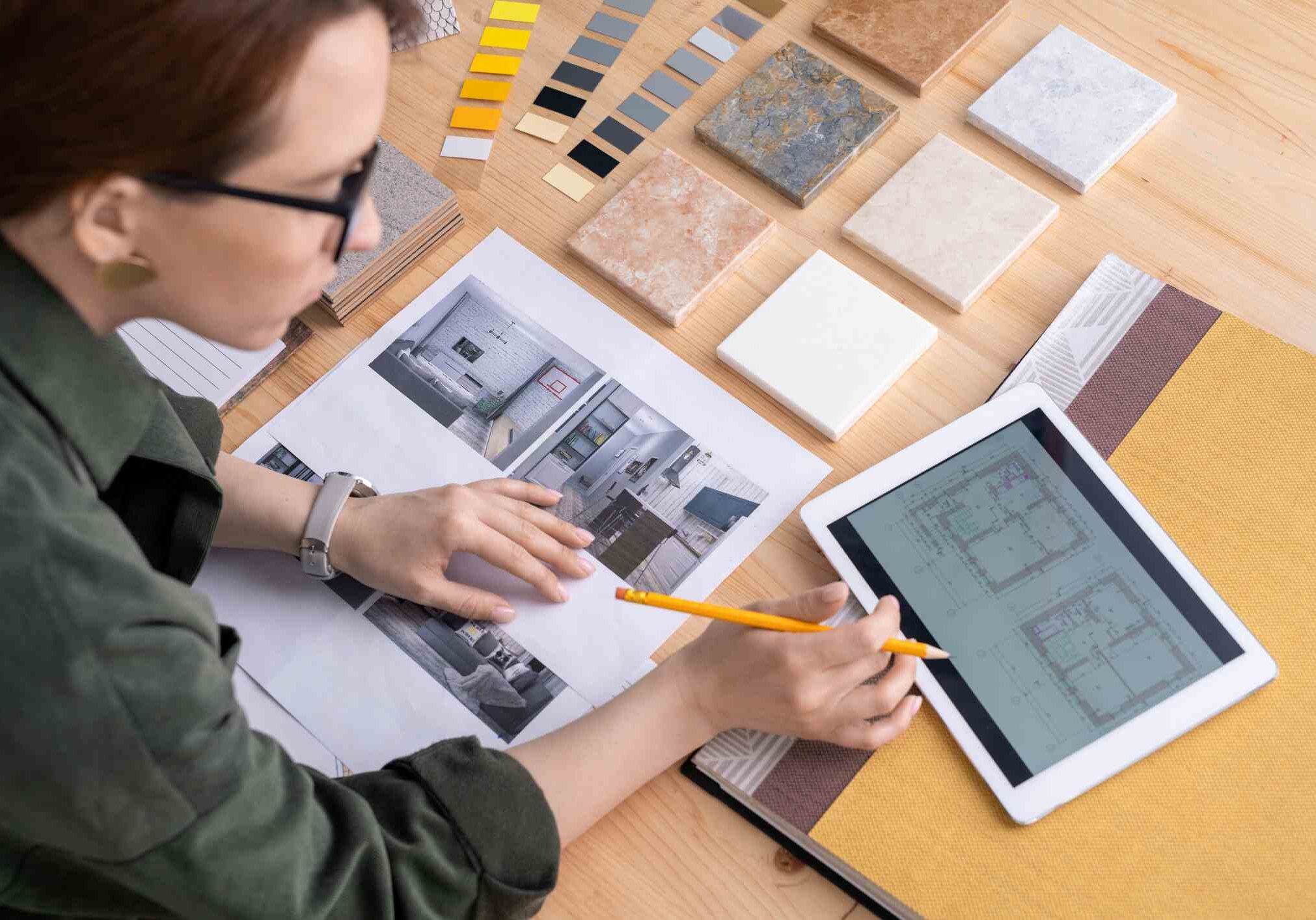 Contemporary young female designer of interior bending over desk while looking through electronic sketches of flat in touchpad