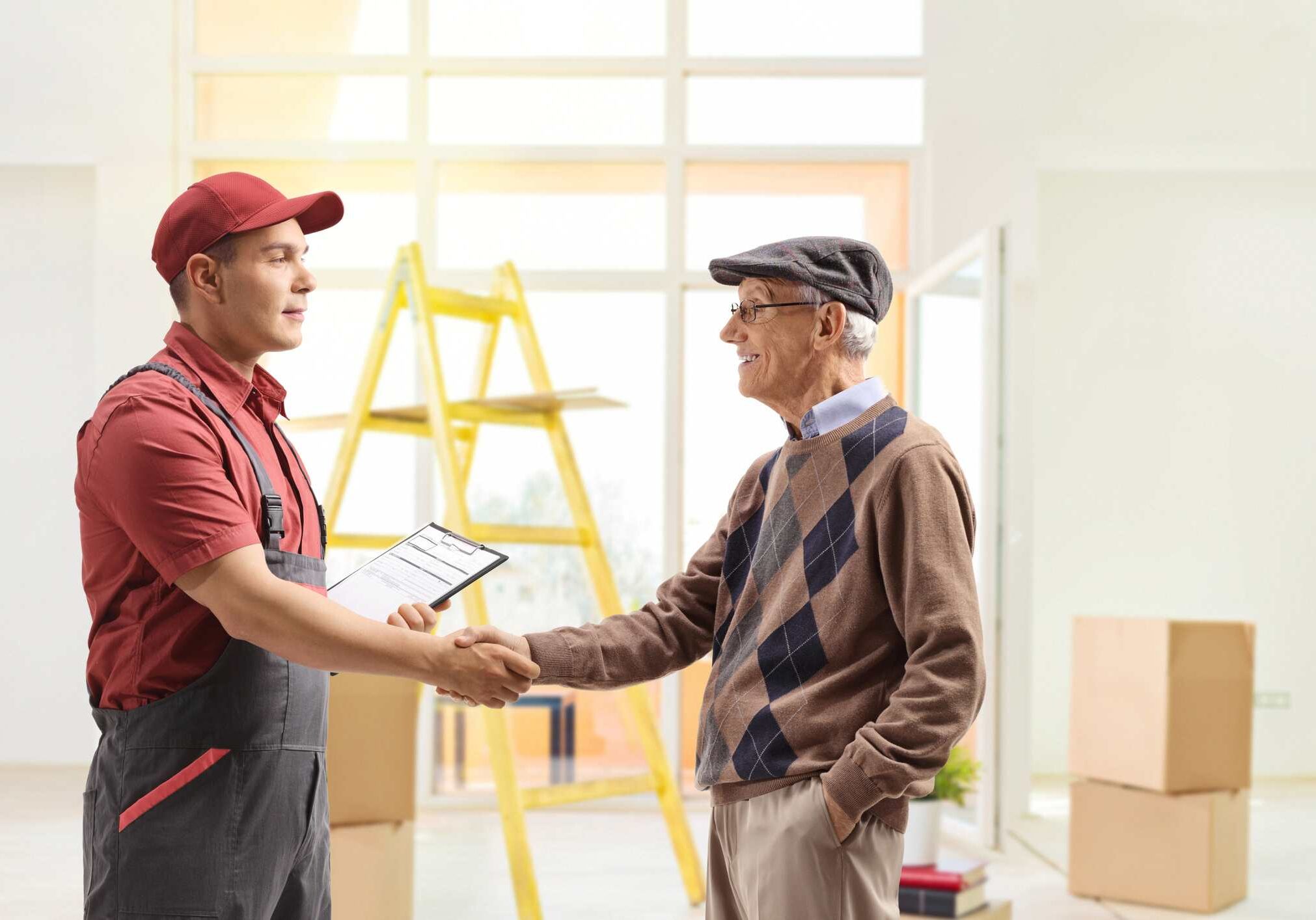 Mover shaking hands with a senior man inside a house