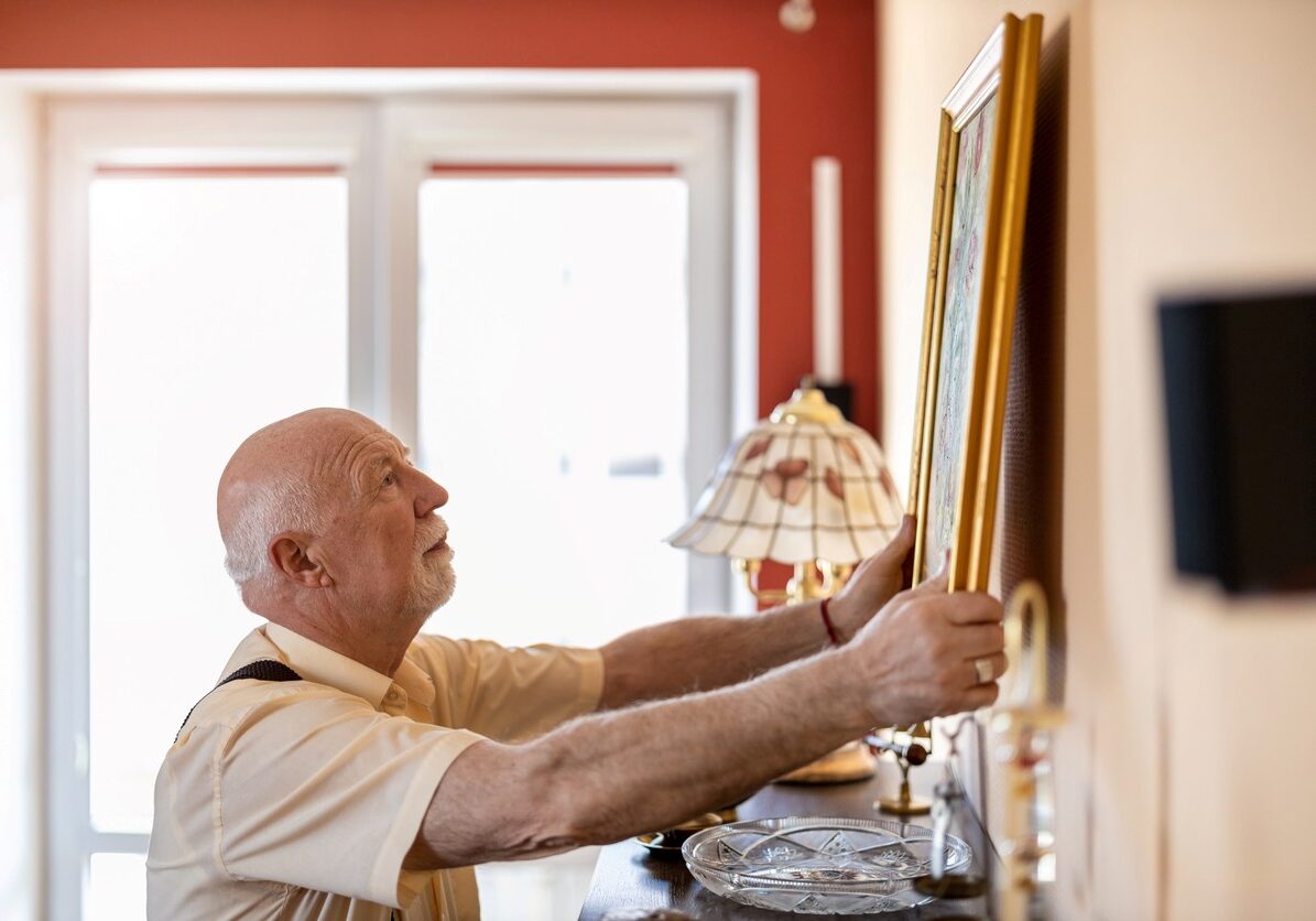 Senior man putting up a painting on the wall at his home