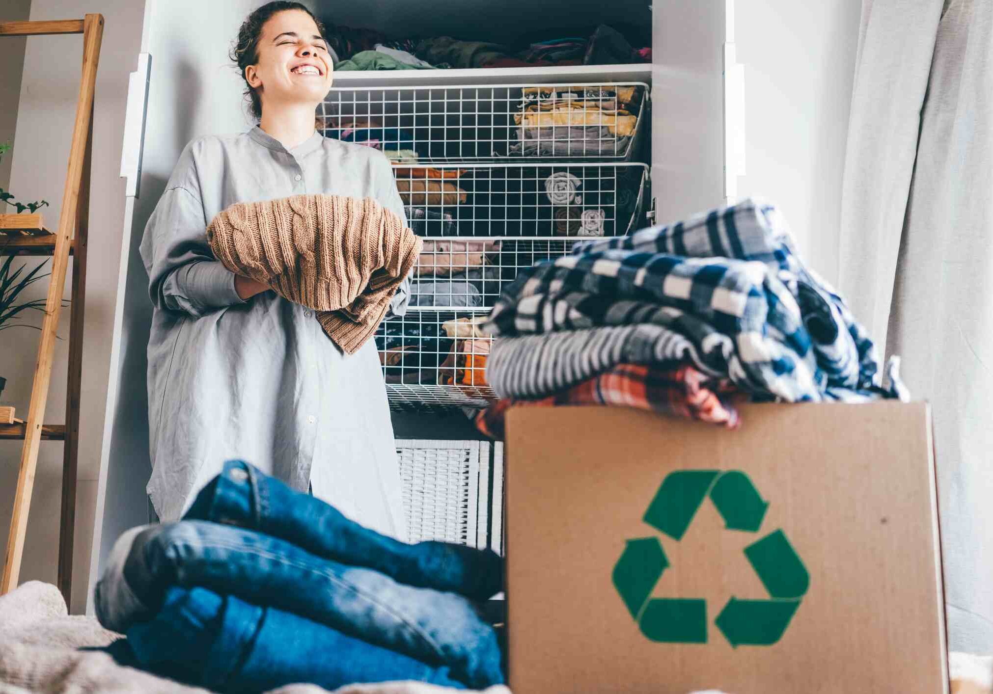 Recycle clothes concept. Young woman with recycling box full clothes.