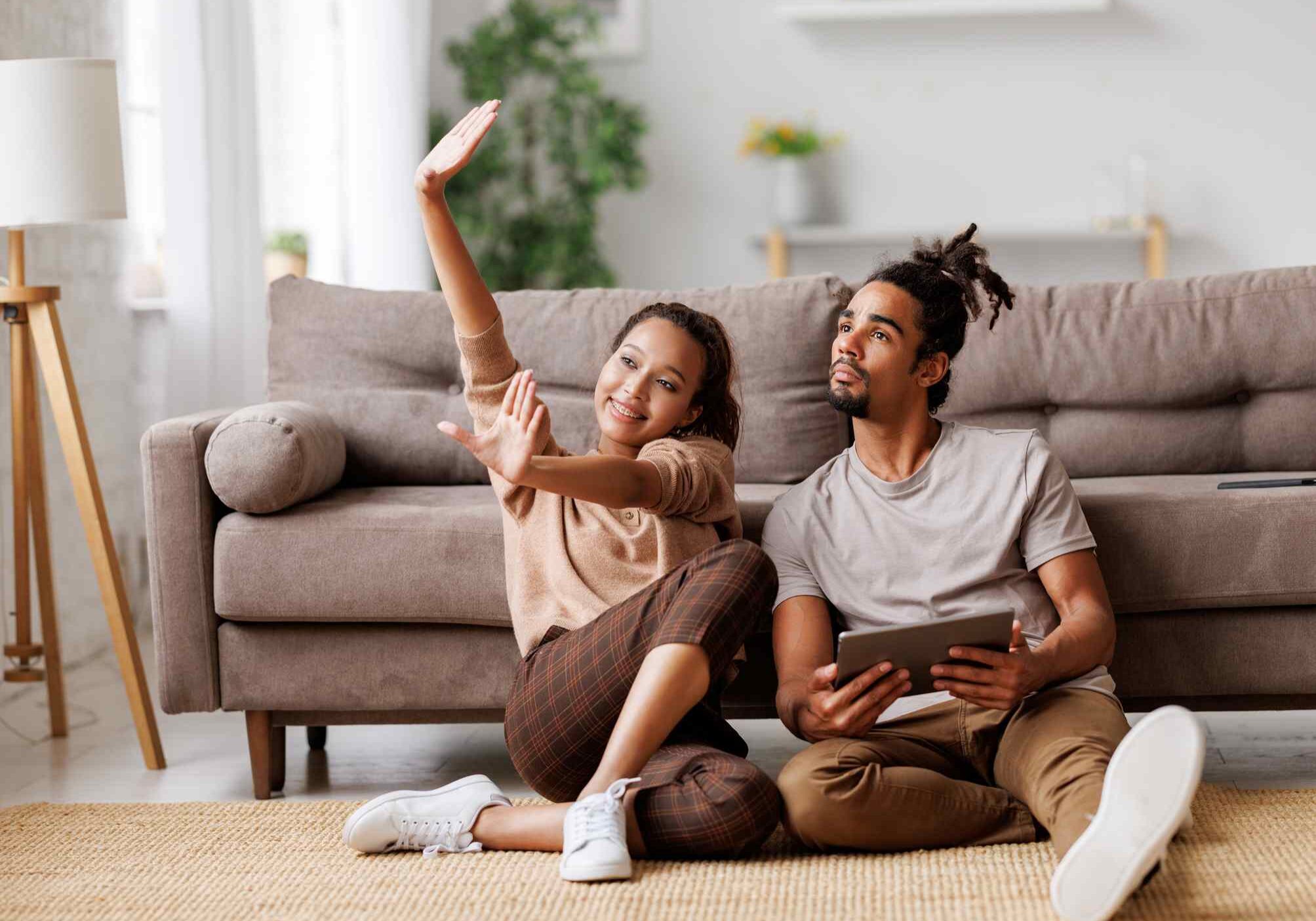 Young lovely african american family couple sitting on floor with digital tablet and discussing new apartment design project or interior design ideas, ethnic man and woman planing home renovation