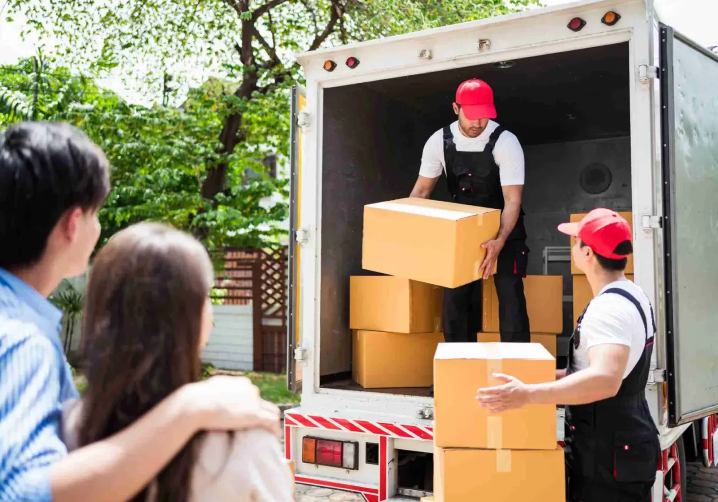 Asian and Caucasian workers in uniform unloading cardboard boxes from the truck. Delivery men unloading boxes and check the checklist with their coworkers. Professional delivery and moving service.