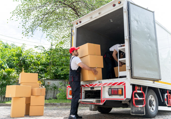 Caucasian young delivery man delivering package to customer at home. Attractive courier postman worker working and loading deliver a box cardboard postal from car truck infront of the house.