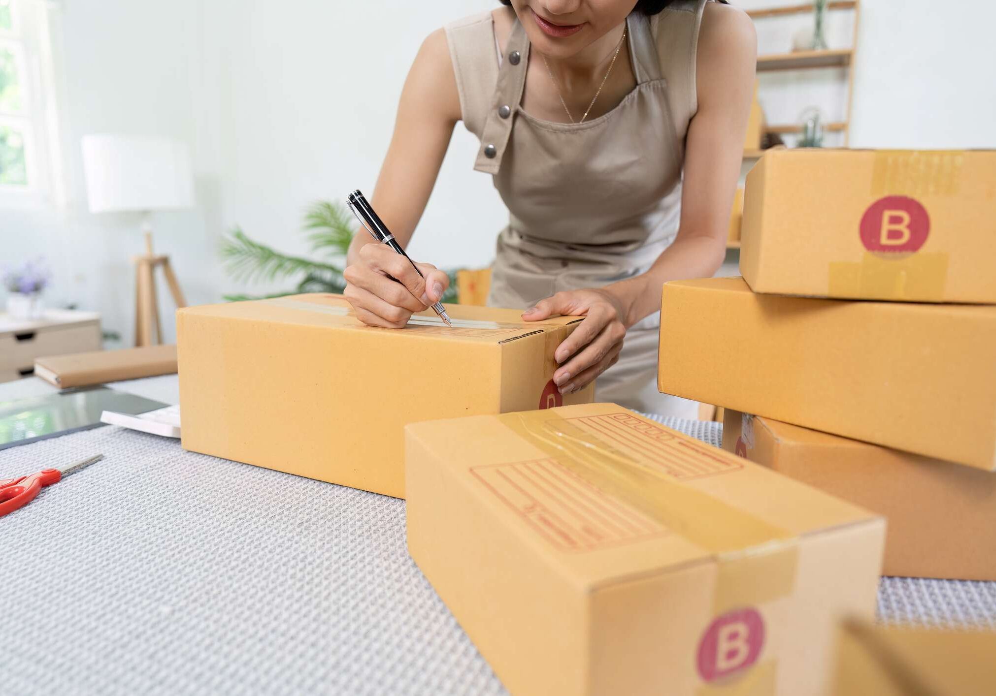 Young asian woman happily prepares orders in her busy office, ensuring smooth delivery for her online shop.