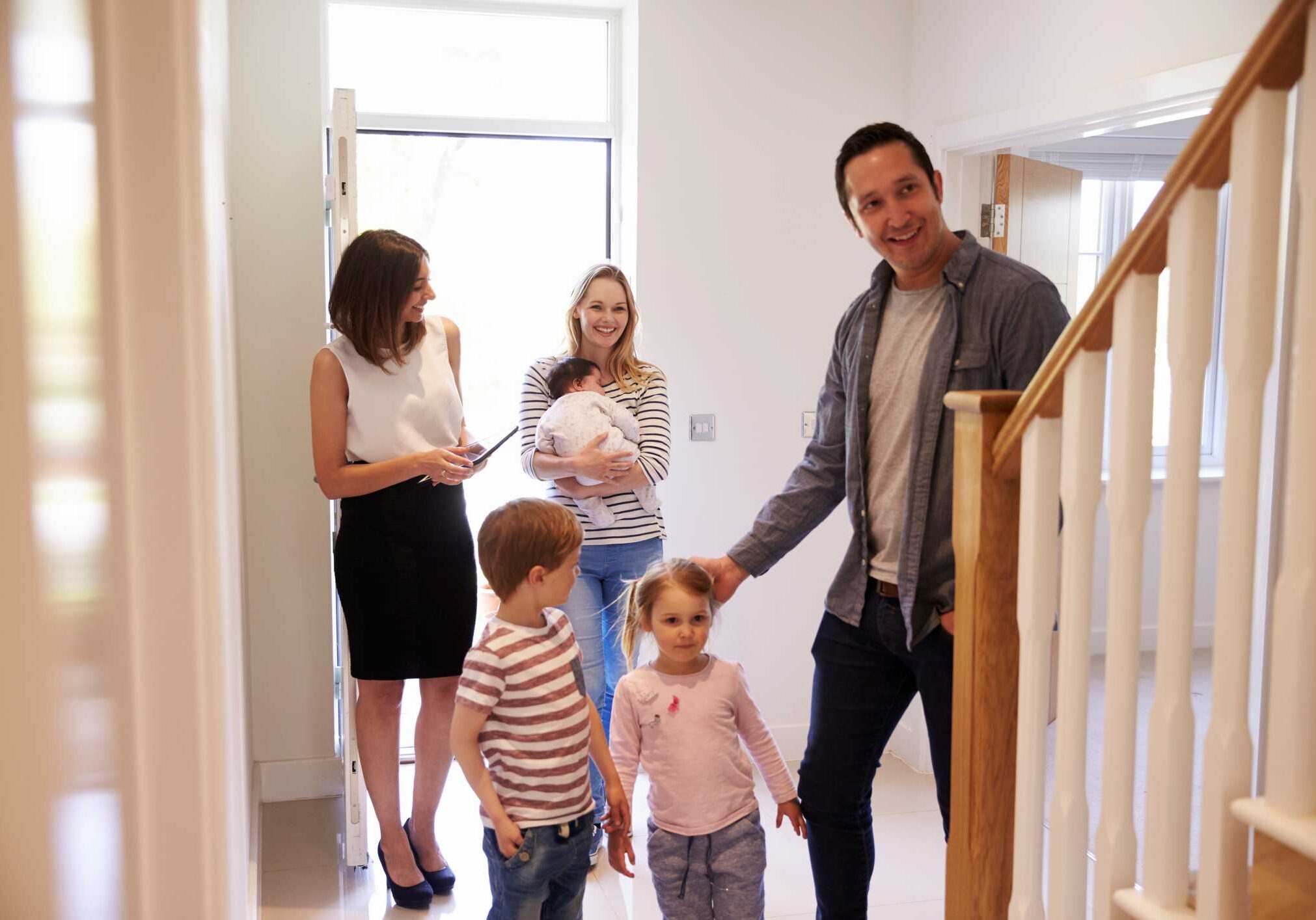 Real Estate Agent Showing Young Family Around Property For Sale